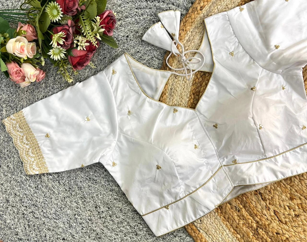 White blouse with gold details on a textured surface with flowers in the background