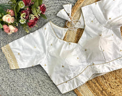 White blouse with gold details on a textured surface with flowers in the background