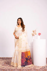 Woman wearing a white saree with a colorful design, standing against a plain background.