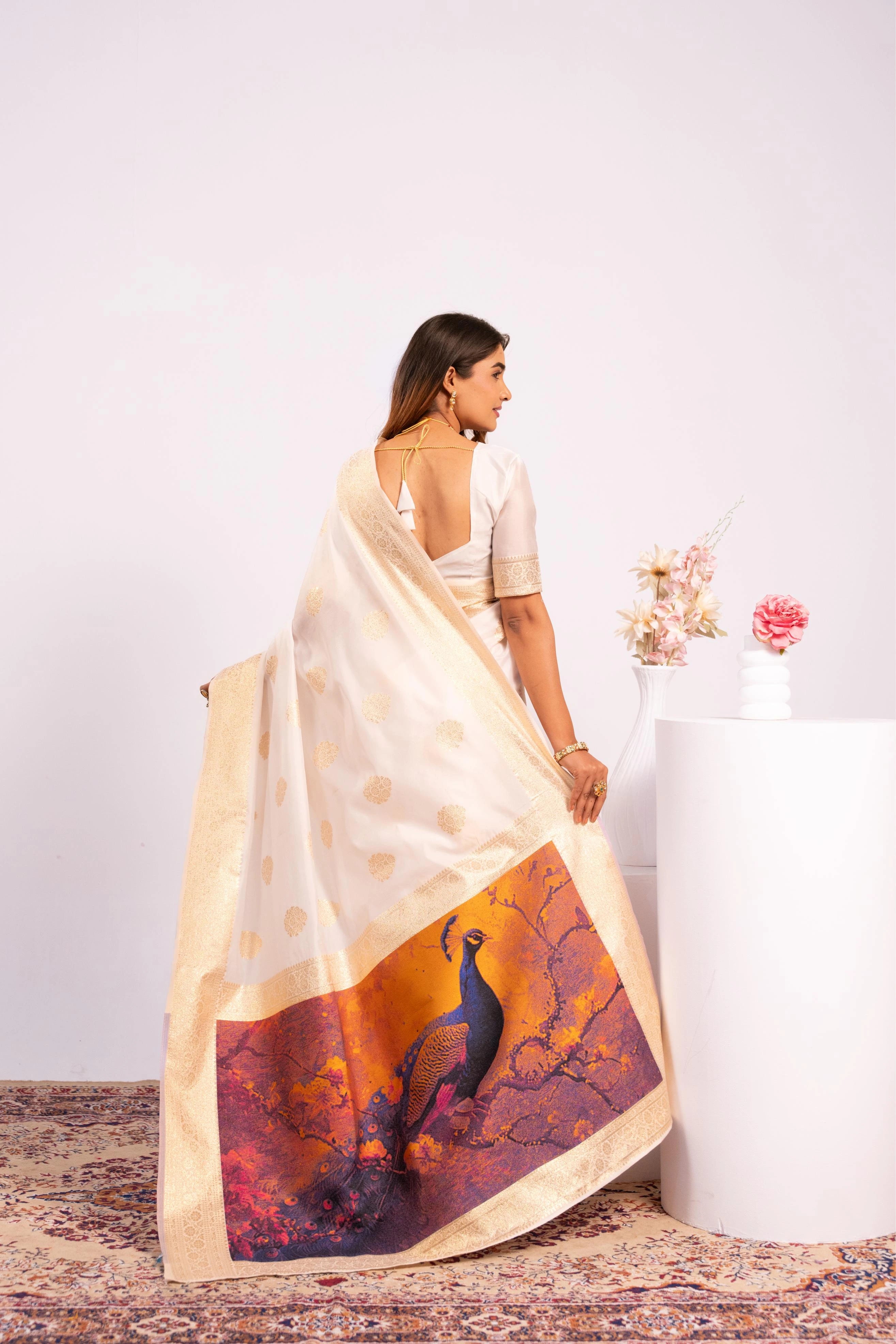Woman holding a white saree with a purple and gold design on a plain background