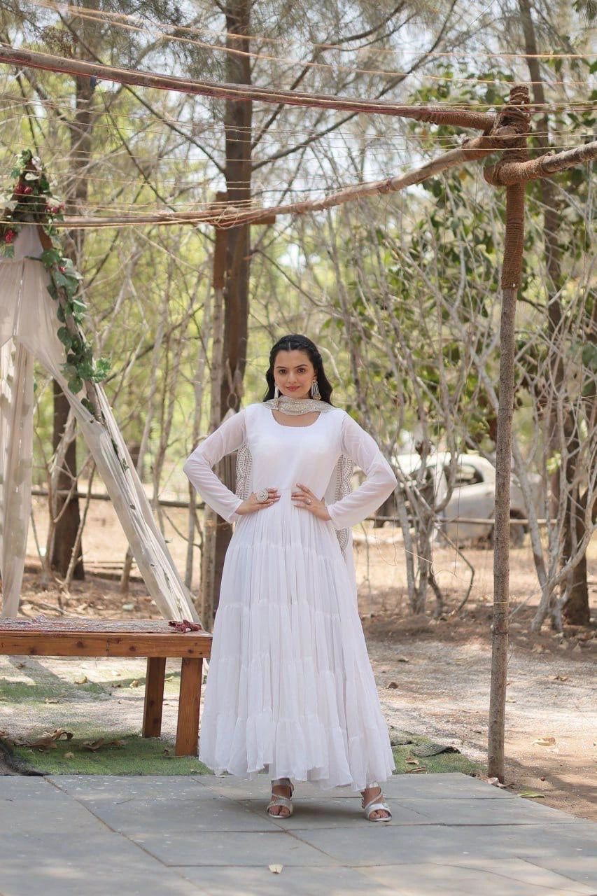 Woman in a white dress standing outdoors with trees and a car in the background