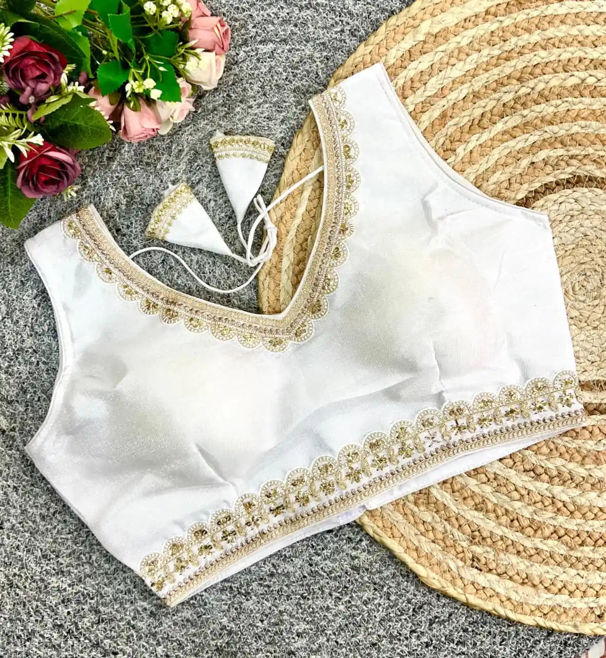 White blouse with gold embroidery on a textured surface with flowers and a fan.