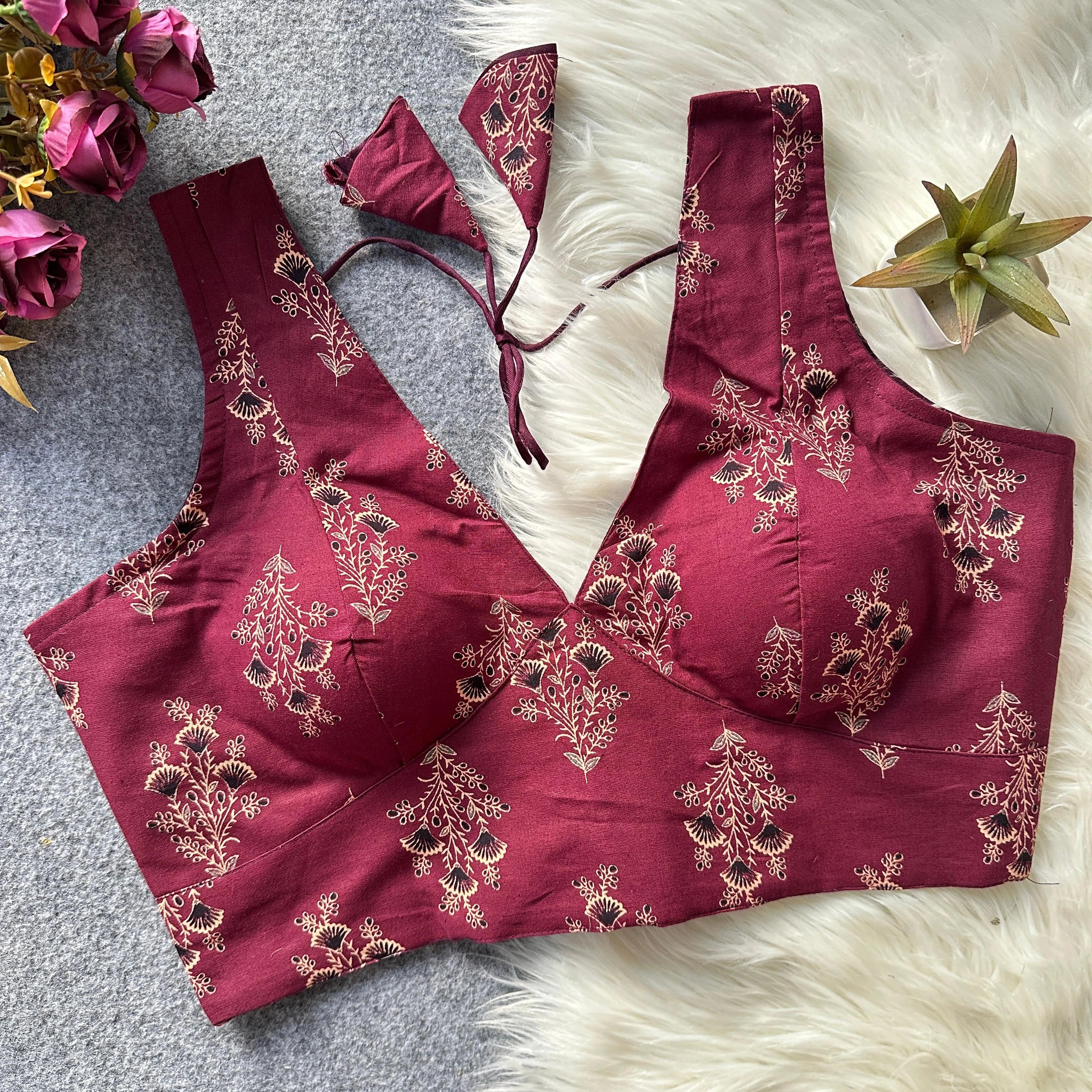 Maroon embroidered blouse with floral patterns on a textured surface with flowers and a plant.
