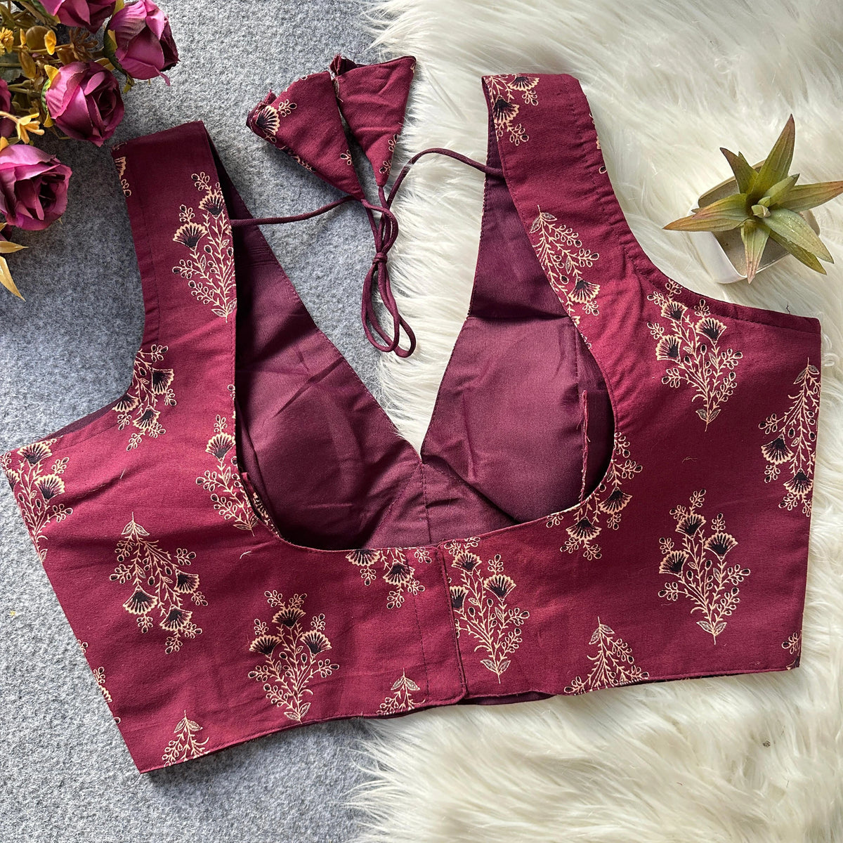 Maroon embroidered blouse with floral patterns on a textured surface with flowers and a plant.