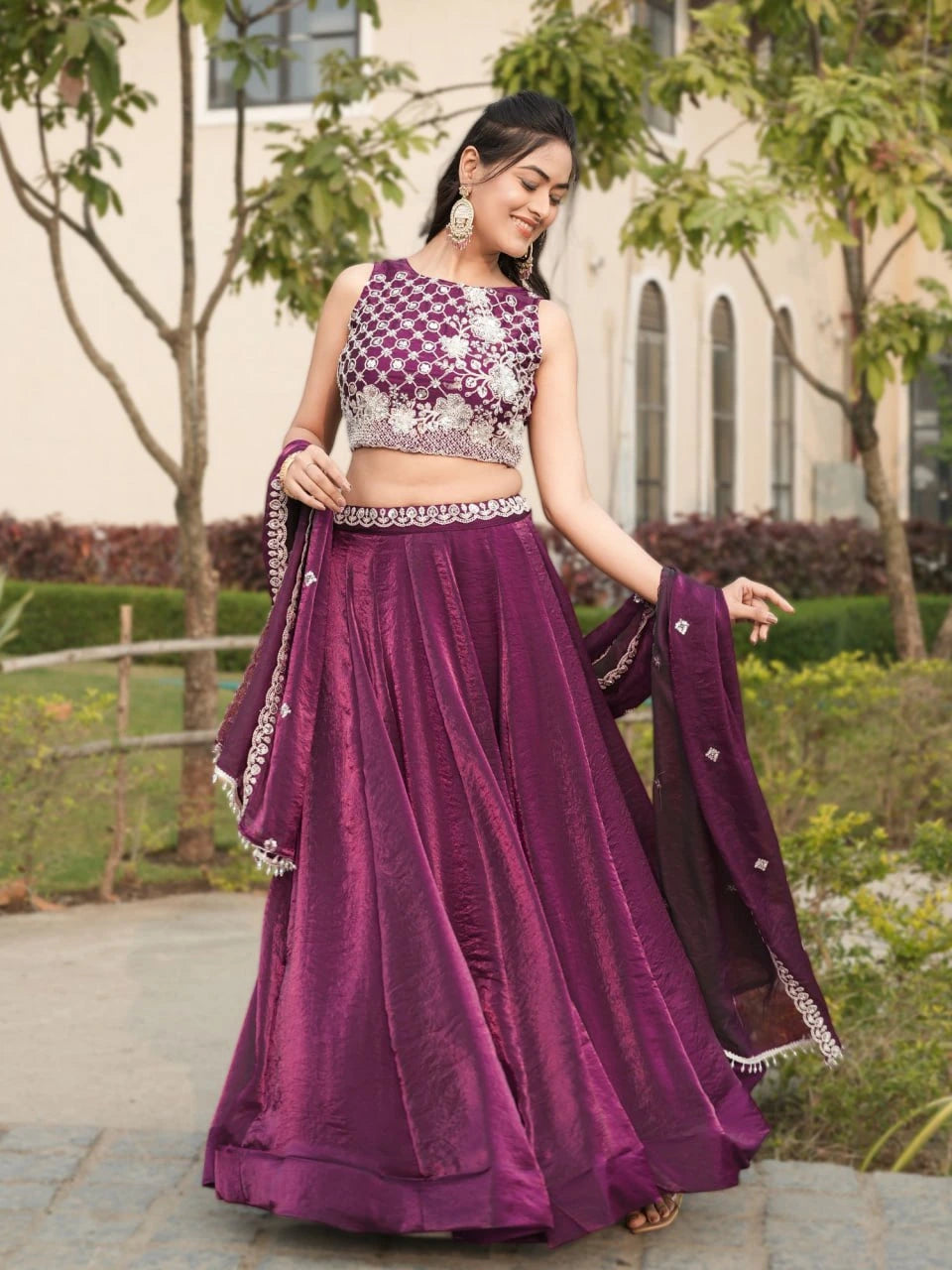 Woman in a purple traditional outfit standing outdoors with greenery in the background