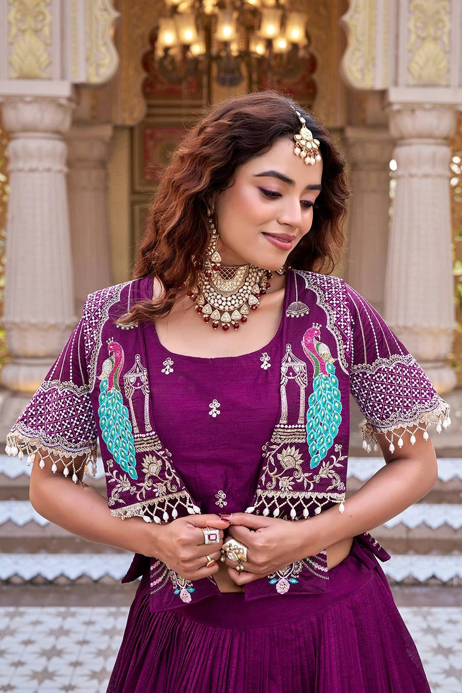 A medium shot showing the woman holding the edges of her magenta open-front jacket. This angle highlights the symmetry of the turquoise peacock embroidery on both sides of the chest and the intricate geometric patterns on the sleeves.