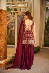 Woman in a maroon traditional outfit with intricate designs, standing indoors.