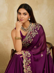 Woman wearing a purple saree with intricate gold embroidery against a beige background
