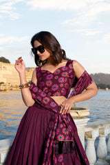 Woman in a purple floral outfit standing by a body of water with a scenic background