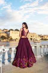 Woman in a purple floral dress standing by a waterfront with a scenic background