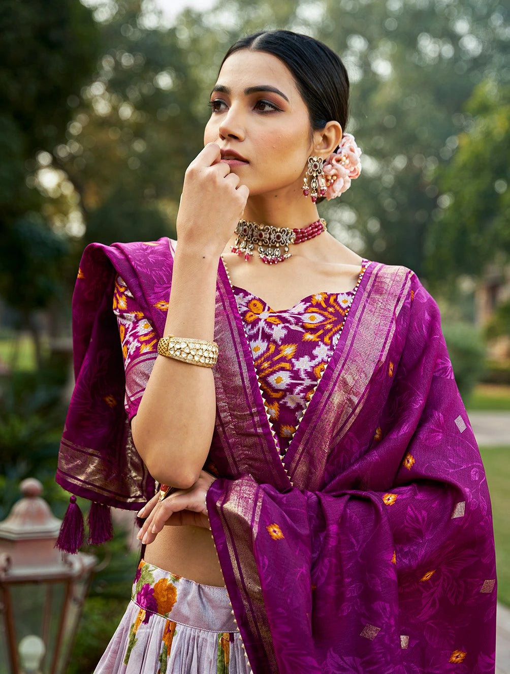 Woman in traditional purple saree with floral jewelry and accessories outdoors