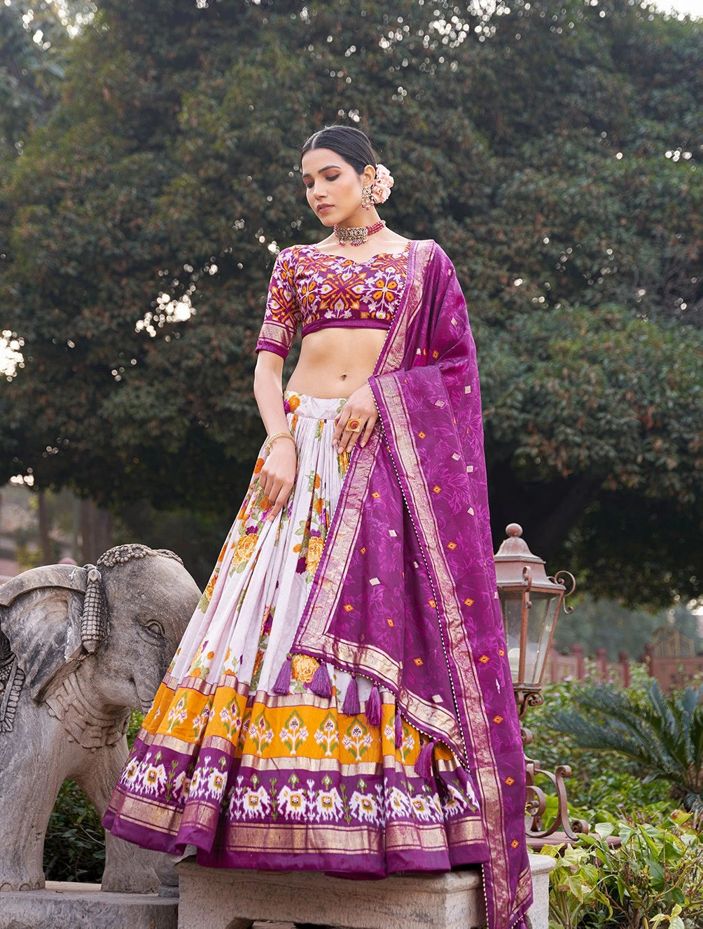 Woman in a traditional outfit with a purple and white patterned dress standing outdoors.