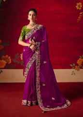 Woman wearing a purple saree with a green blouse against a red floral background