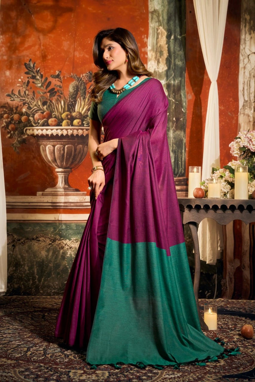 Woman wearing a purple and green saree in an ornate room with decorative elements.