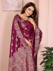 Woman wearing a maroon saree with intricate patterns, standing against a light pink wall.