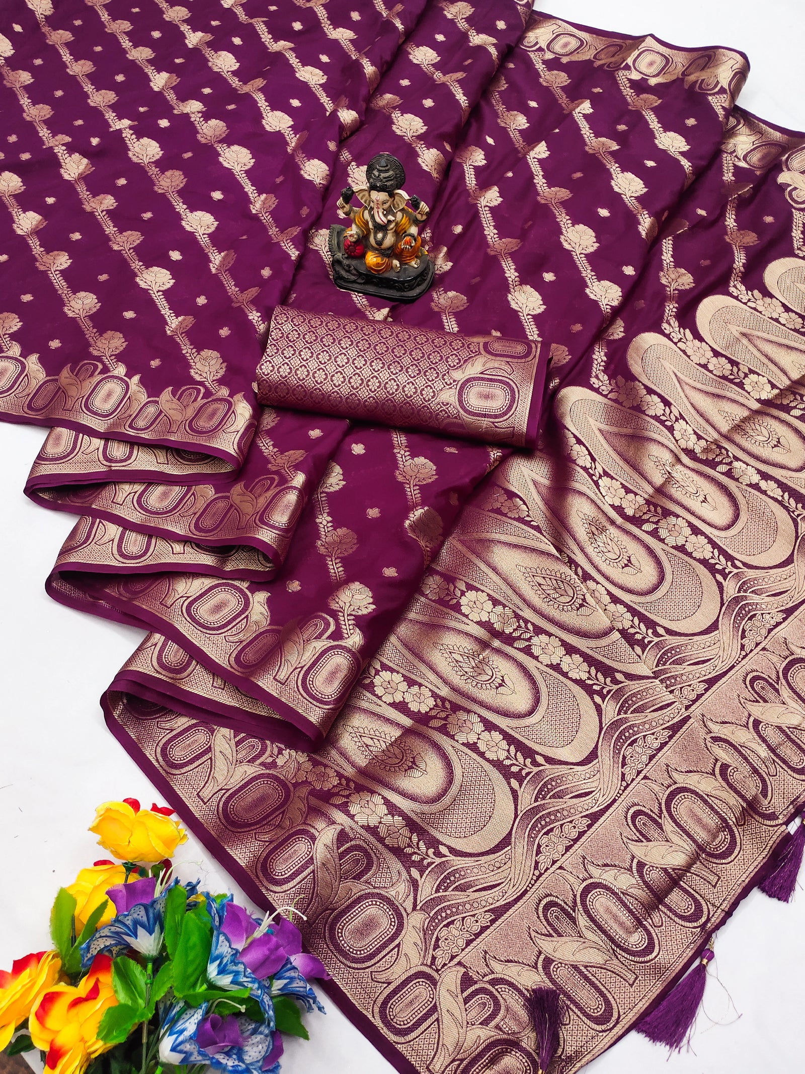 Purple saree with gold patterns, a small statue, and flowers on a white background
