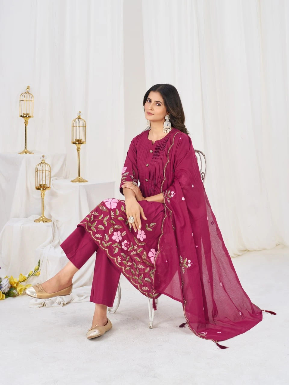 Woman in a magenta traditional outfit with floral patterns sitting on a white chair.