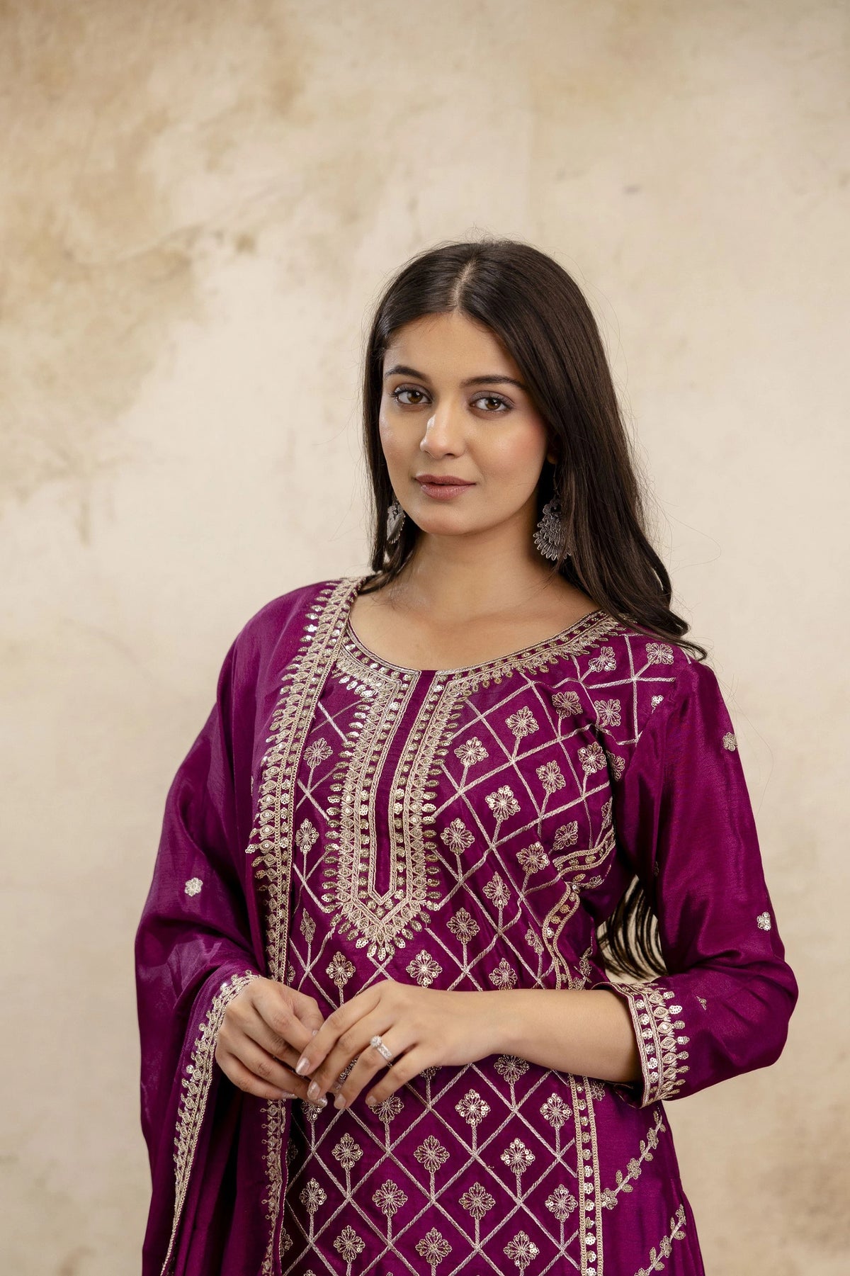 Woman wearing a purple embroidered traditional outfit against a beige background