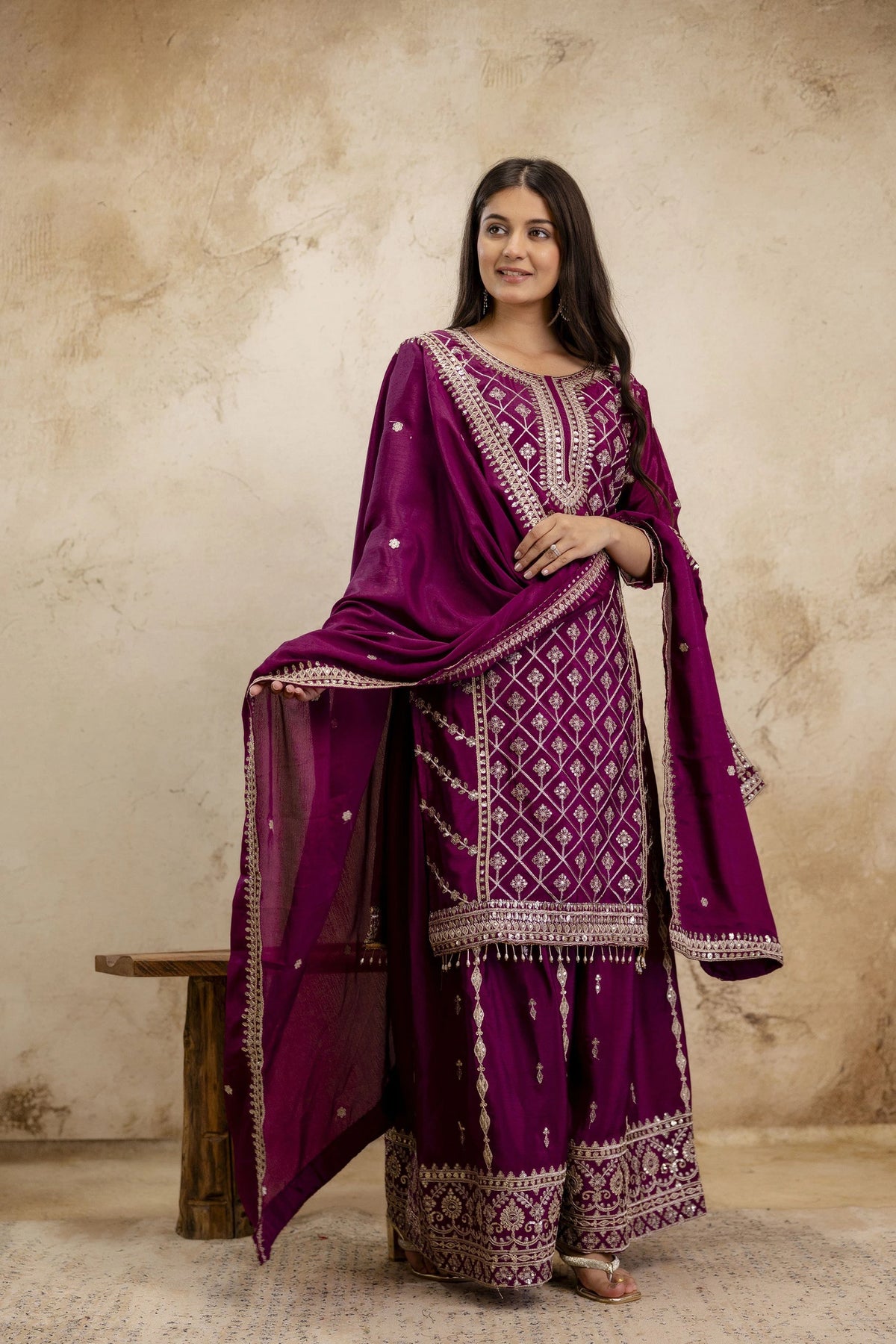 Woman wearing a traditional purple outfit with intricate patterns against a beige background