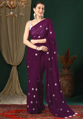 Woman wearing a purple saree with white patterns in a decorated indoor setting.