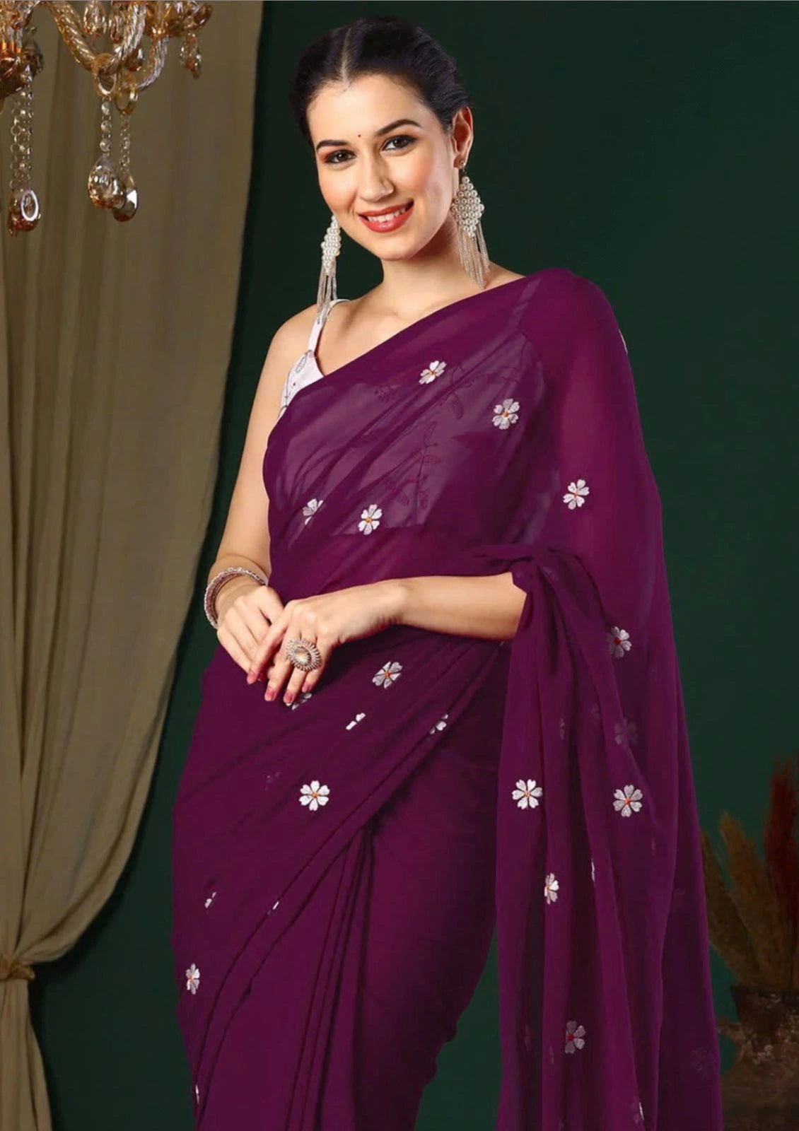 Woman wearing a purple saree with white floral patterns against a green background