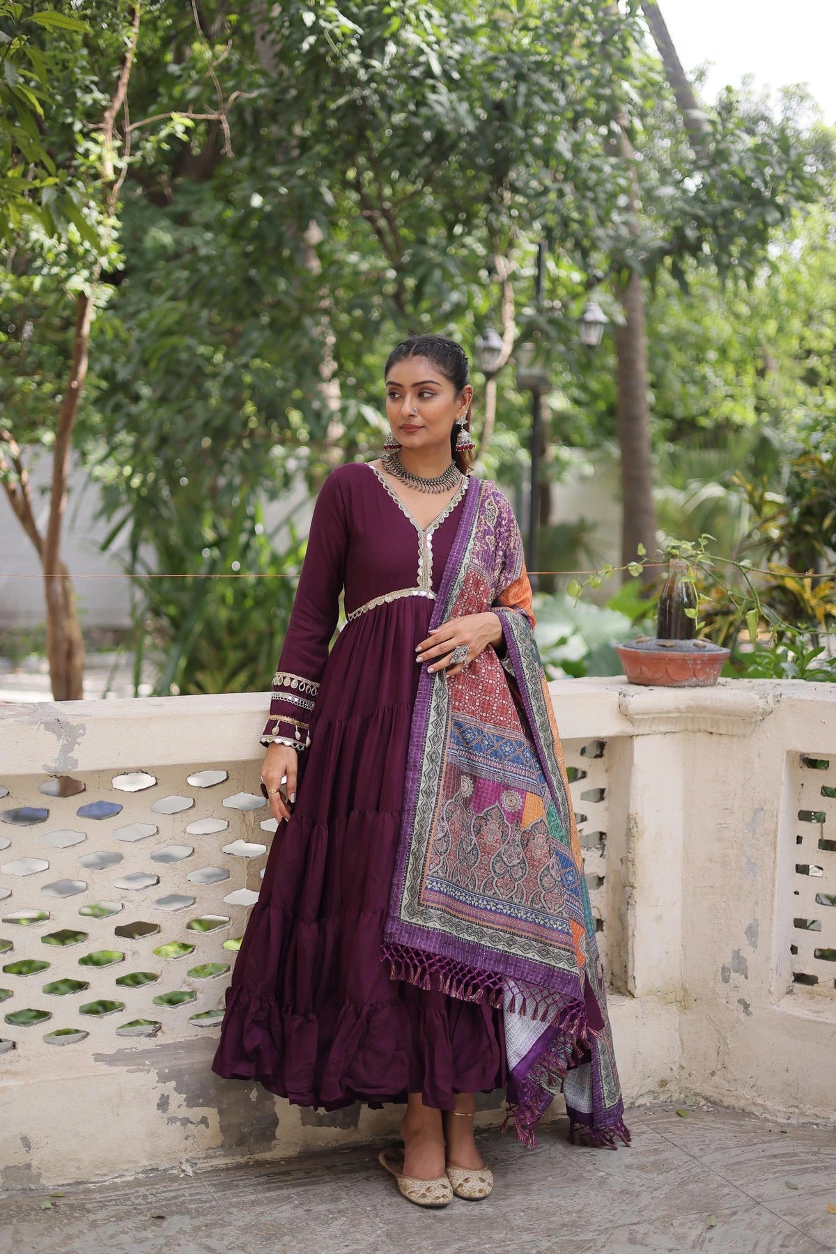 Woman in a purple traditional outfit with a colorful scarf standing outdoors.