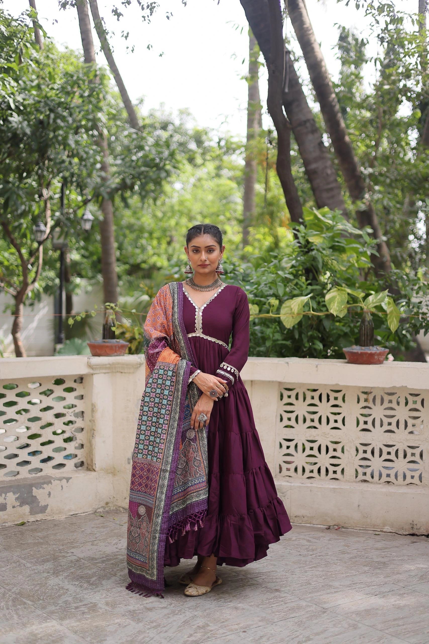 Woman in a purple traditional outfit standing on a balcony with greenery in the background