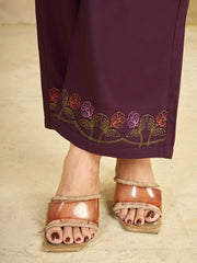 Purple garment with floral embroidery worn by a person wearing brown sandals on a beige background