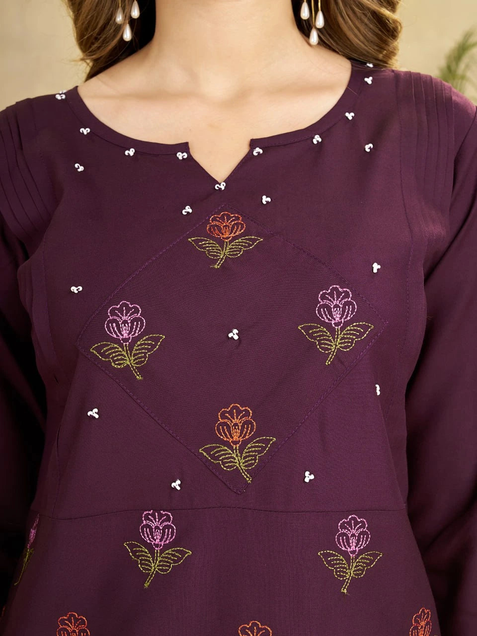 Close-up of a purple garment with floral embroidery and bead details.