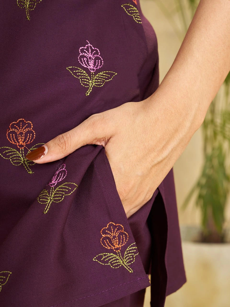 Close-up of a person wearing a purple dress with floral embroidery, with a blurred natural background.