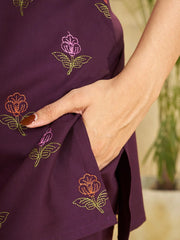 Close-up of a person wearing a purple dress with floral embroidery, with a blurred natural background.