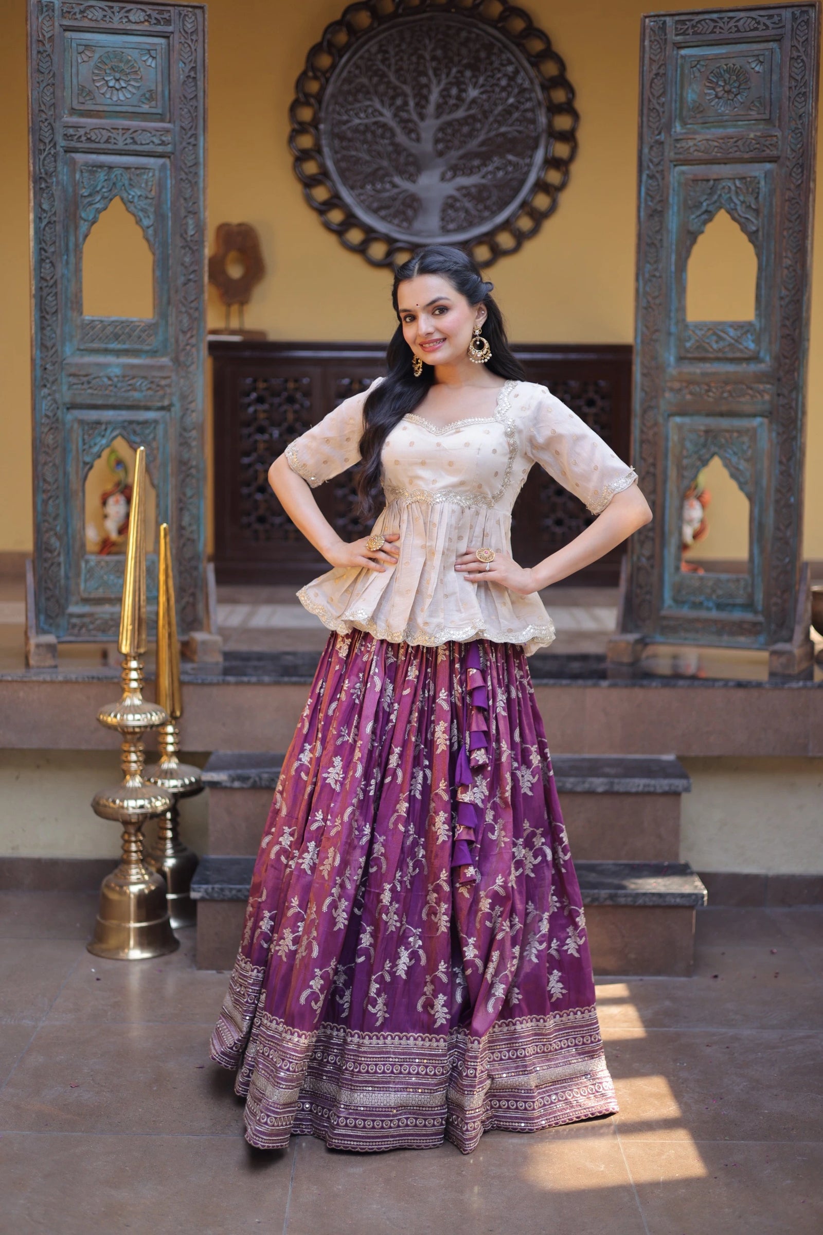 Woman in traditional outfit with purple skirt and white top in a decorated room.