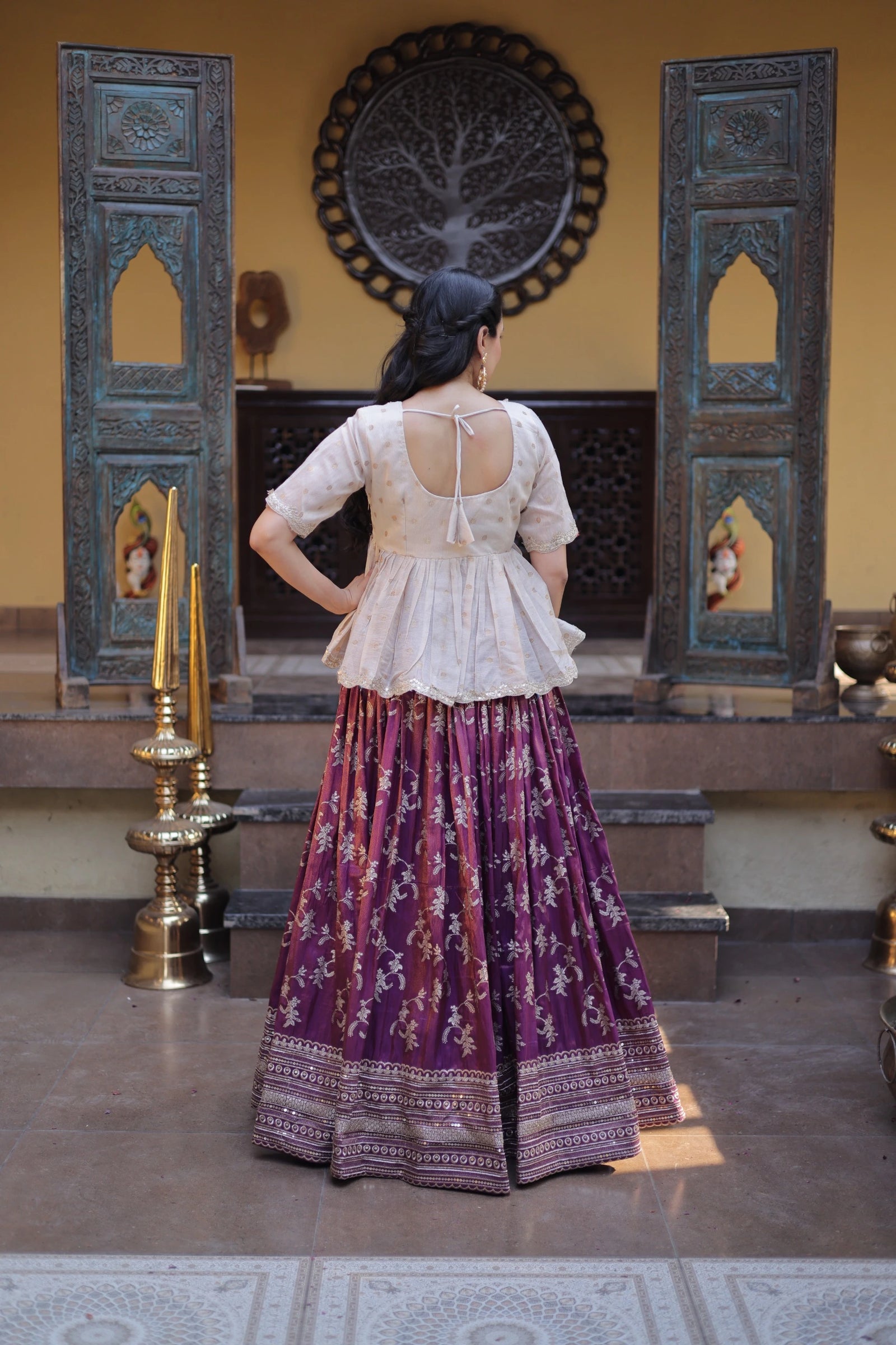 Woman wearing a white top and purple patterned skirt in a decorative setting.