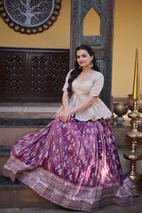 Woman in a traditional outfit with a purple skirt and white top, standing in an ornate indoor setting.