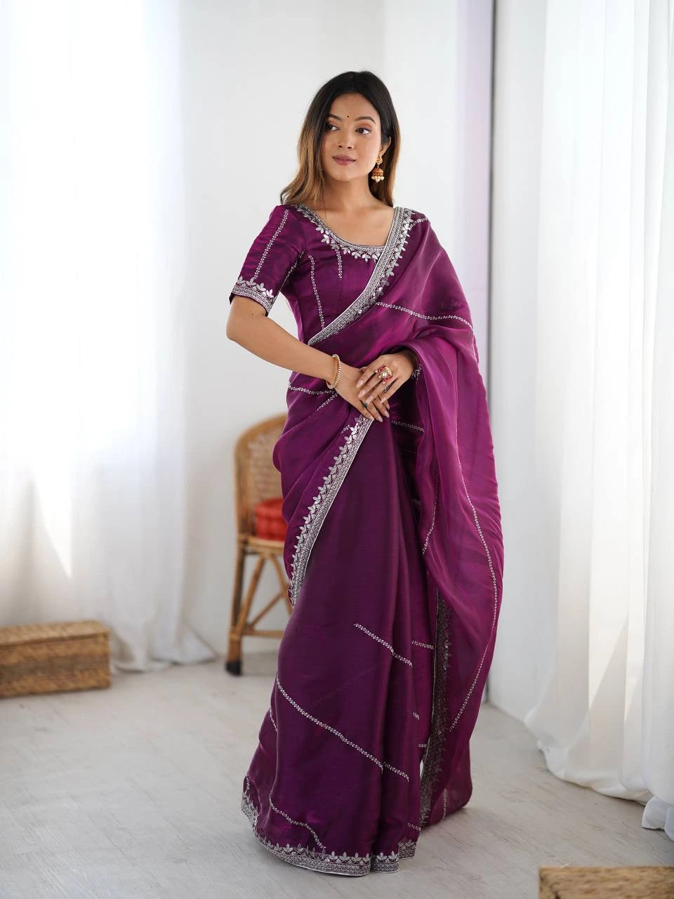 Woman wearing a purple saree with silver border indoors.
