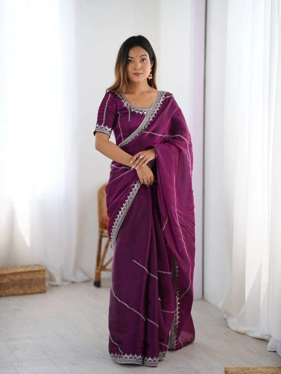 Woman wearing a purple saree with white patterns in a minimalistic room.