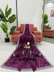 Purple embroidered fabric with a small figurine on a white surface, with a red sofa and green plants in the background.