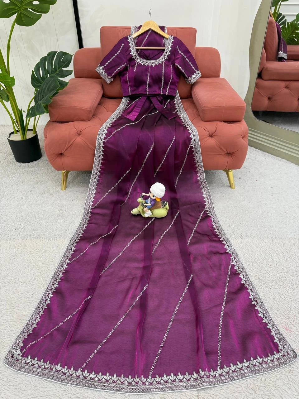 Purple saree with silver border on a pink sofa with a plant in the background