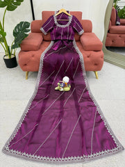 Purple saree with silver border on a pink sofa with a plant in the background