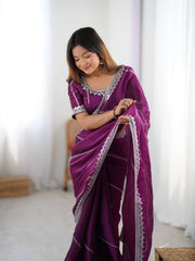 Woman wearing a purple saree with white patterns indoors.