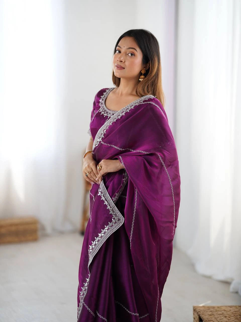 Woman wearing a purple saree with white embroidery in a bright room.