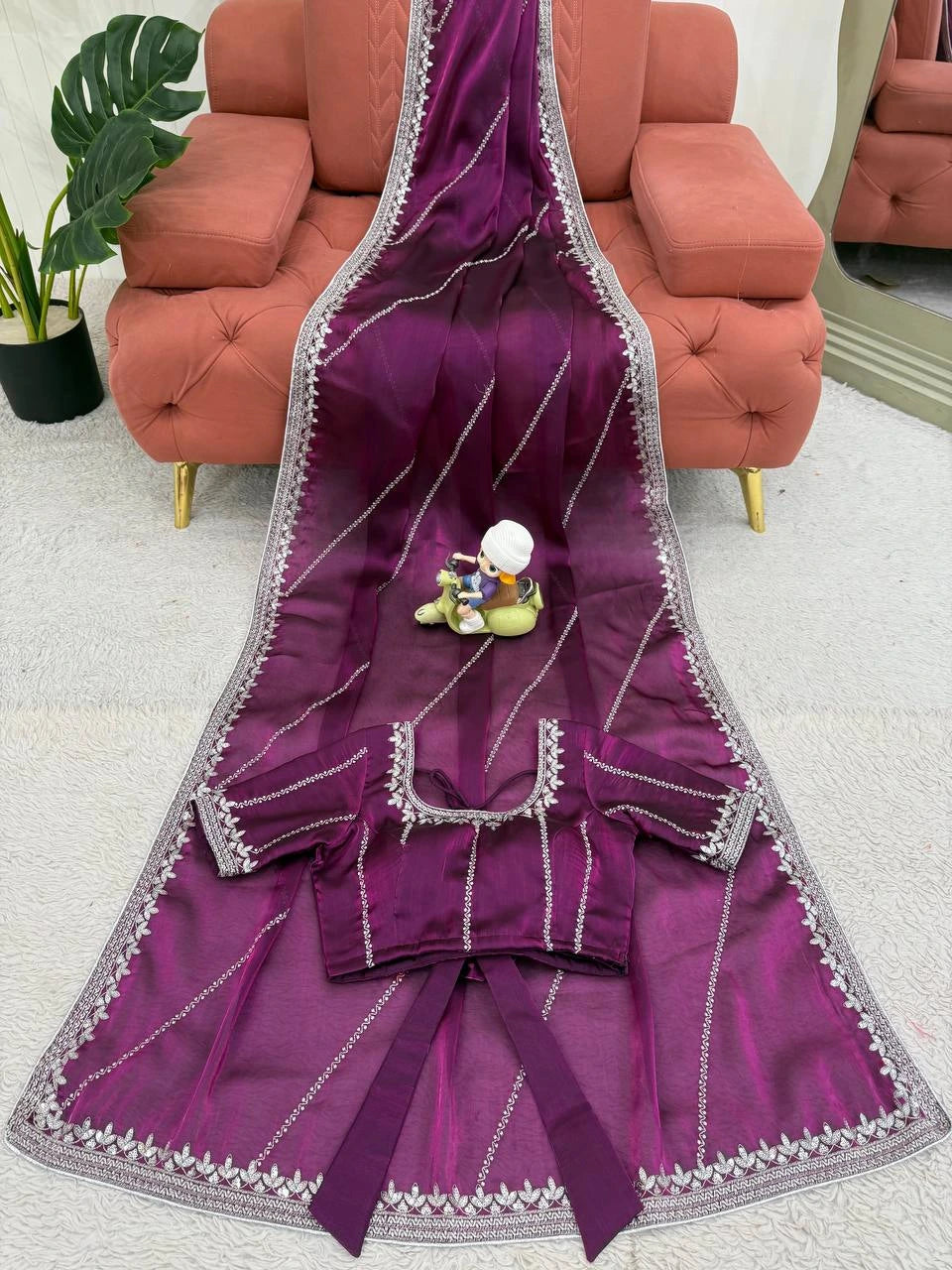 Purple saree with silver border on a light gray floor with a pink sofa in the background