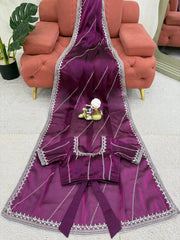 Purple saree with silver border on a light gray floor with a pink sofa in the background