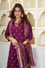 Woman wearing a traditional outfit with a purple top and patterned scarf against a decorative wall.