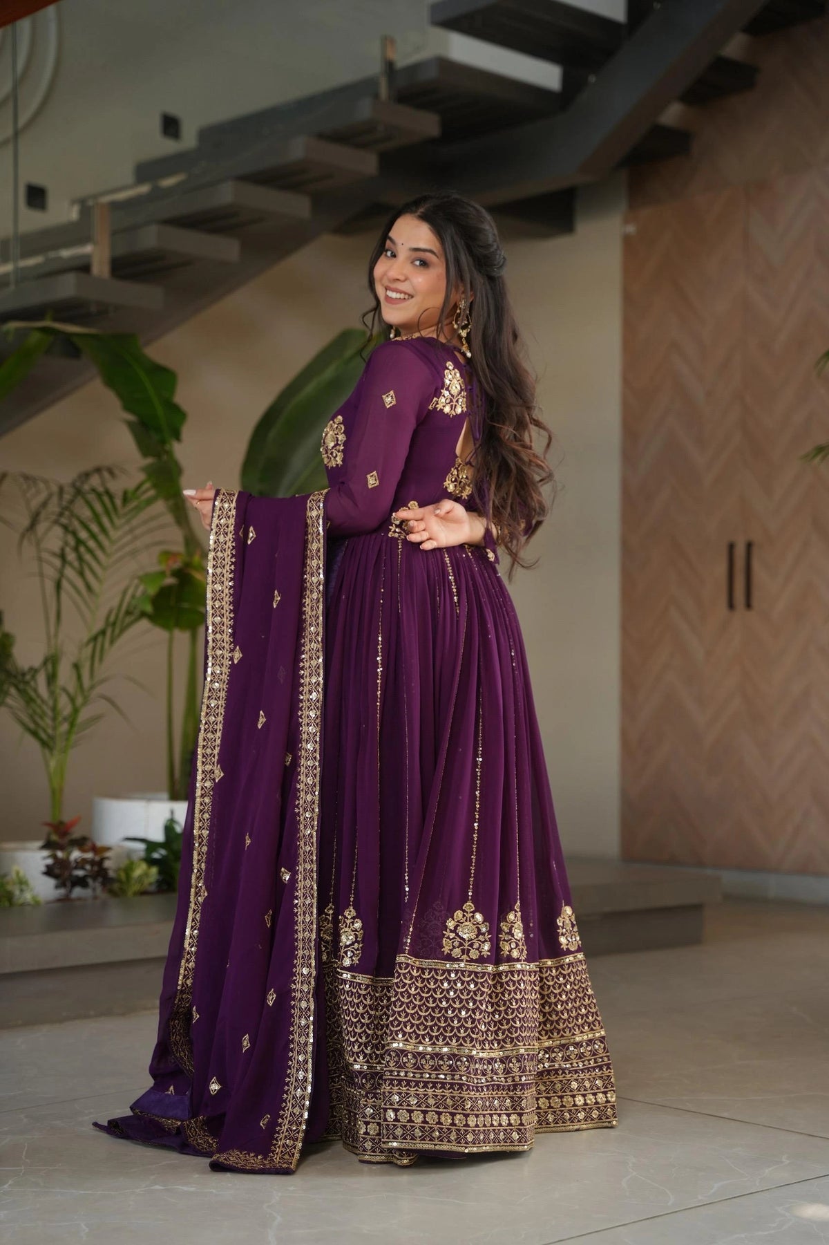 Woman in a purple traditional outfit with gold embroidery standing indoors.