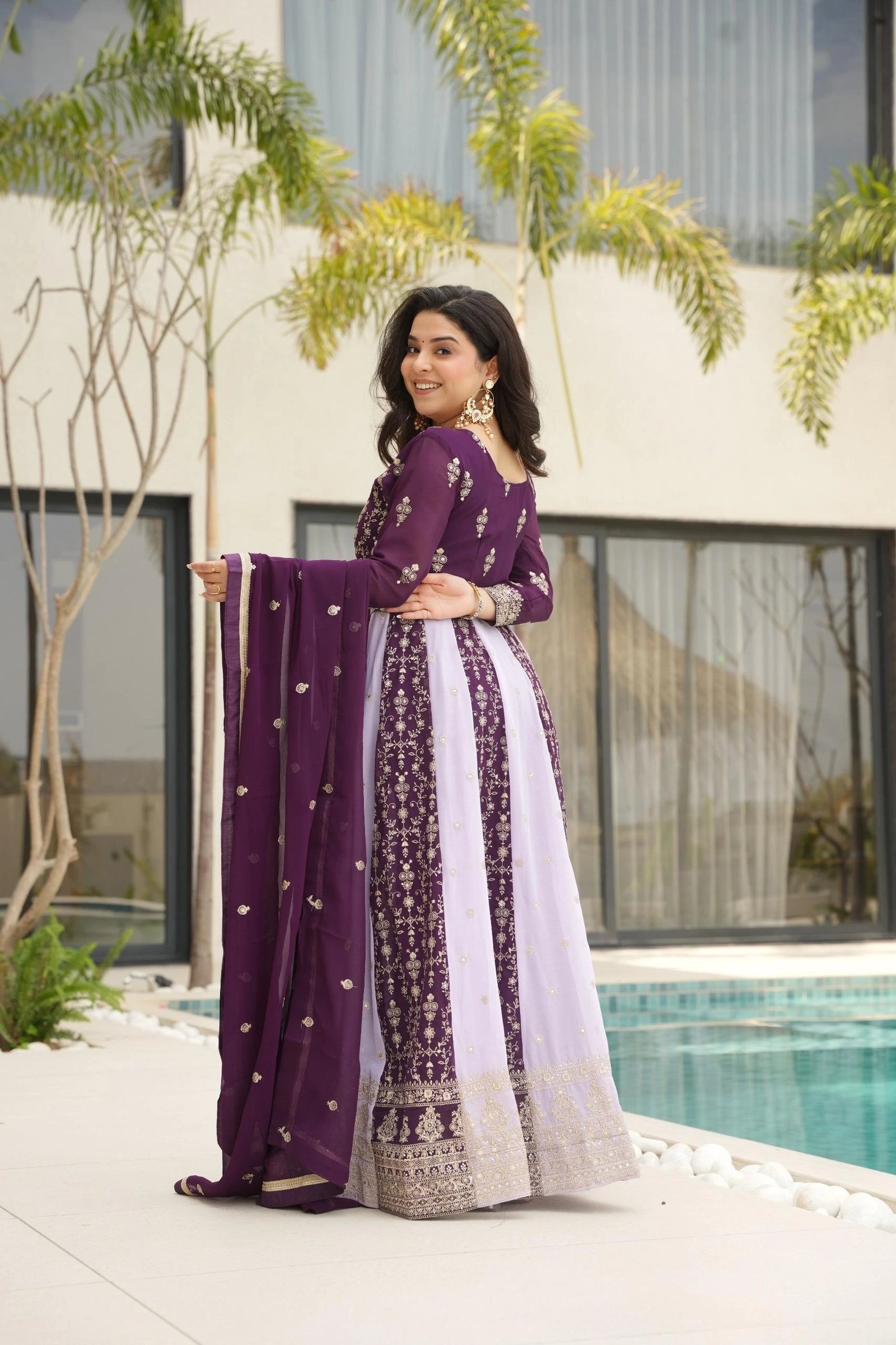 Woman in a purple and white traditional outfit standing by a pool.