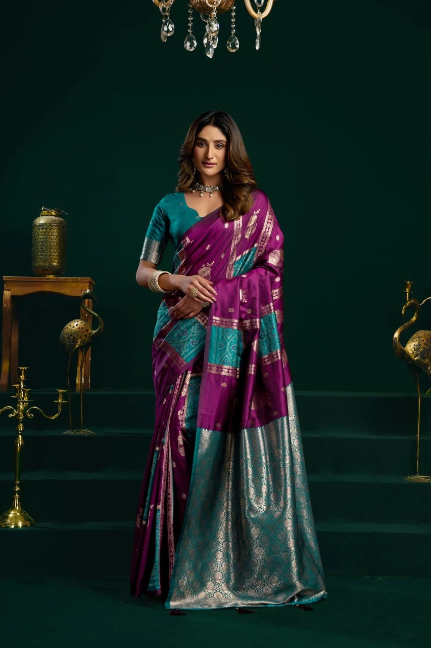 Woman in a purple and blue saree standing in a decorated room with dark green walls.