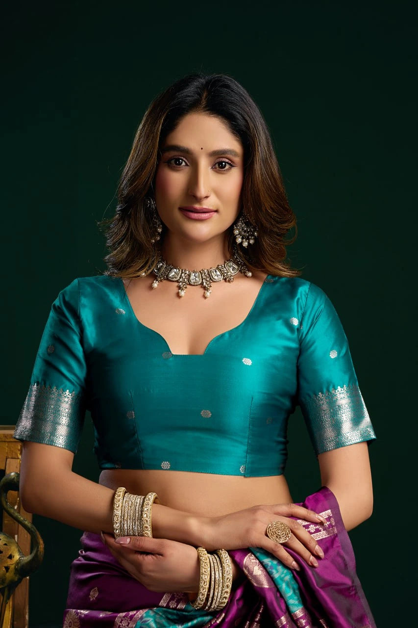 Woman wearing a teal blouse with silver details and a purple saree against a dark background