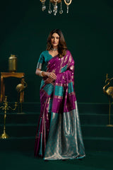 Woman in a purple and blue saree standing in a decorated room with dark green walls.