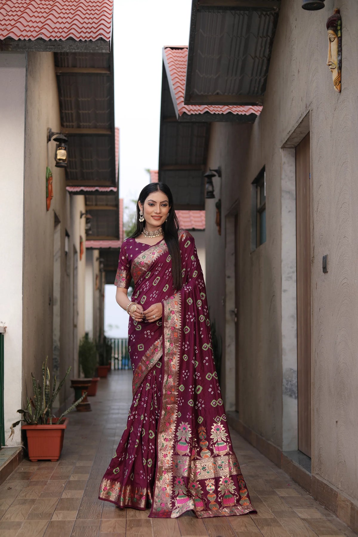 Woman in a traditional maroon saree with floral patterns standing in a narrow alleyway.